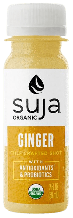 Suja Ginger Shot bottle on a table surrounded by fresh ginger, apples, and oranges, showcasing its immune-boosting and health-enhancing ingredients