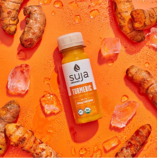 Suja Turmeric Shot bottle surrounded by fresh turmeric, ginger, and other natural ingredients